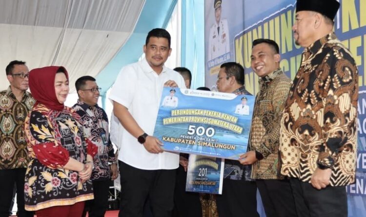 Penyerahan simbolis klaim Jaminan Kematian dan Jaminan Kecelakaan Kerja kepada penerima manfaat dari Gubsu Bobby Nasution kepada Wakil Bupati Simalungun Benny Sinaga.(Simantab/ist)
