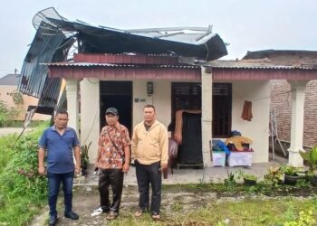 Pemilik rumah korban cuaca ektrem,S Rajagukguk (kanan), Lurah Tanjung Pinggir dan Sekretaris Lurah berfoto di depan rumah yang nyaris tak beratap lagi.(Simantab/Sitanggang)