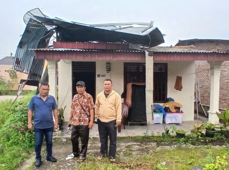 Pemilik rumah korban cuaca ektrem,S Rajagukguk (kanan), Lurah Tanjung Pinggir dan Sekretaris Lurah berfoto di depan rumah yang nyaris tak beratap lagi.(Simantab/Sitanggang)