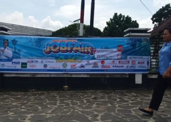 Seorang mahasiswi berjalan melewati spanduk Job Fair Pematangsiantar 2025 di di halaman Universitas HKBP Nommensen. (Simantab/Putra Purba)